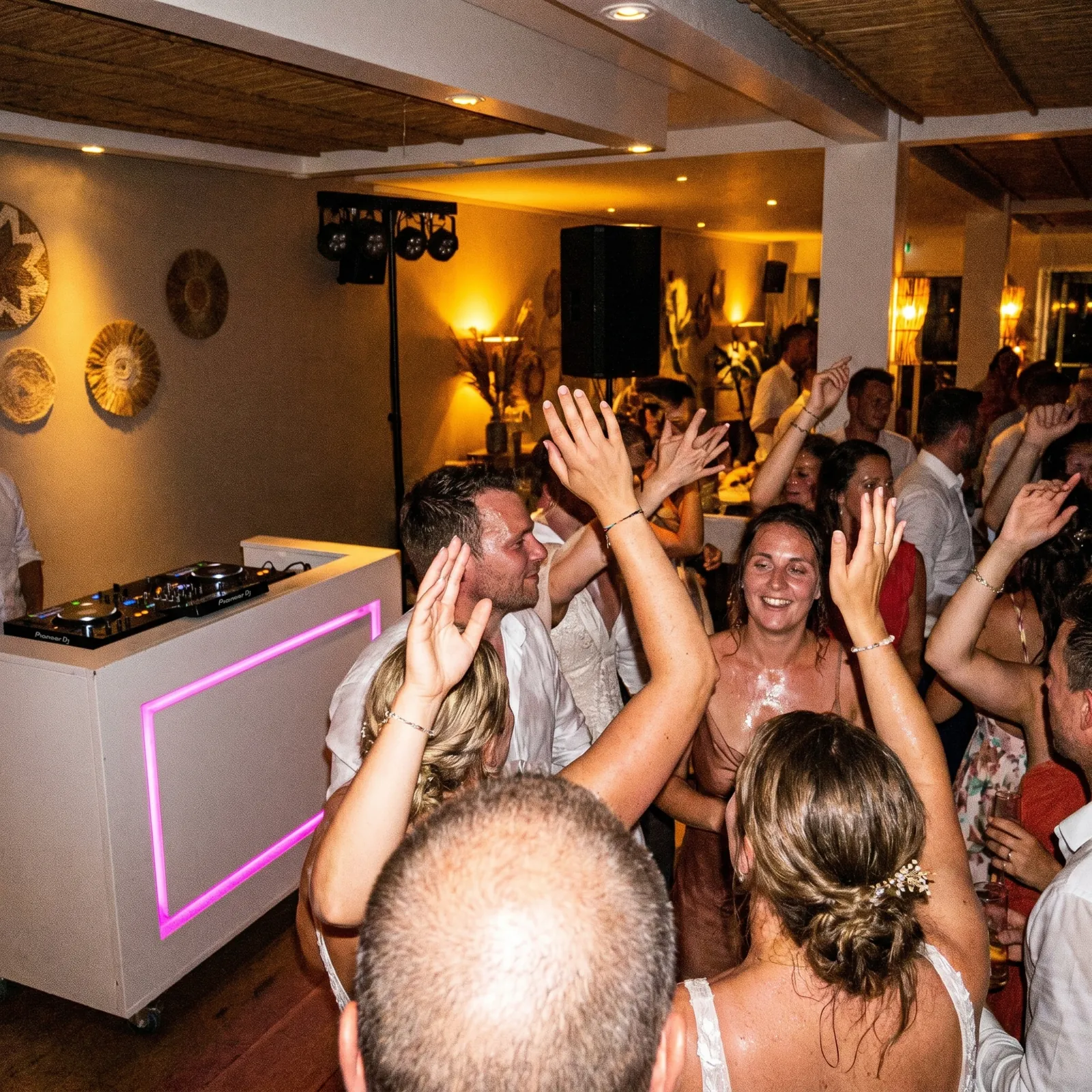 Juichende gasten bij een DJ-booth met roze verlichting
