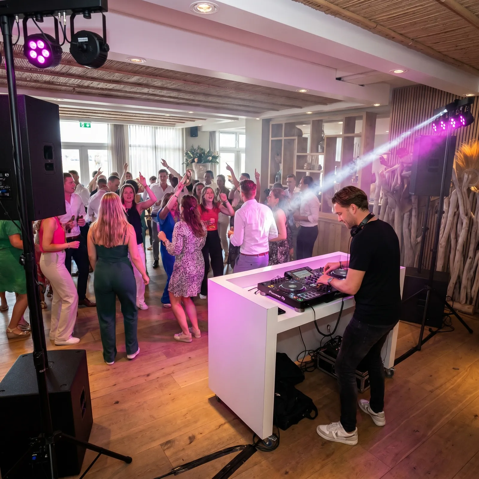 Feest met paarse verlichting rond een witte DJ-booth