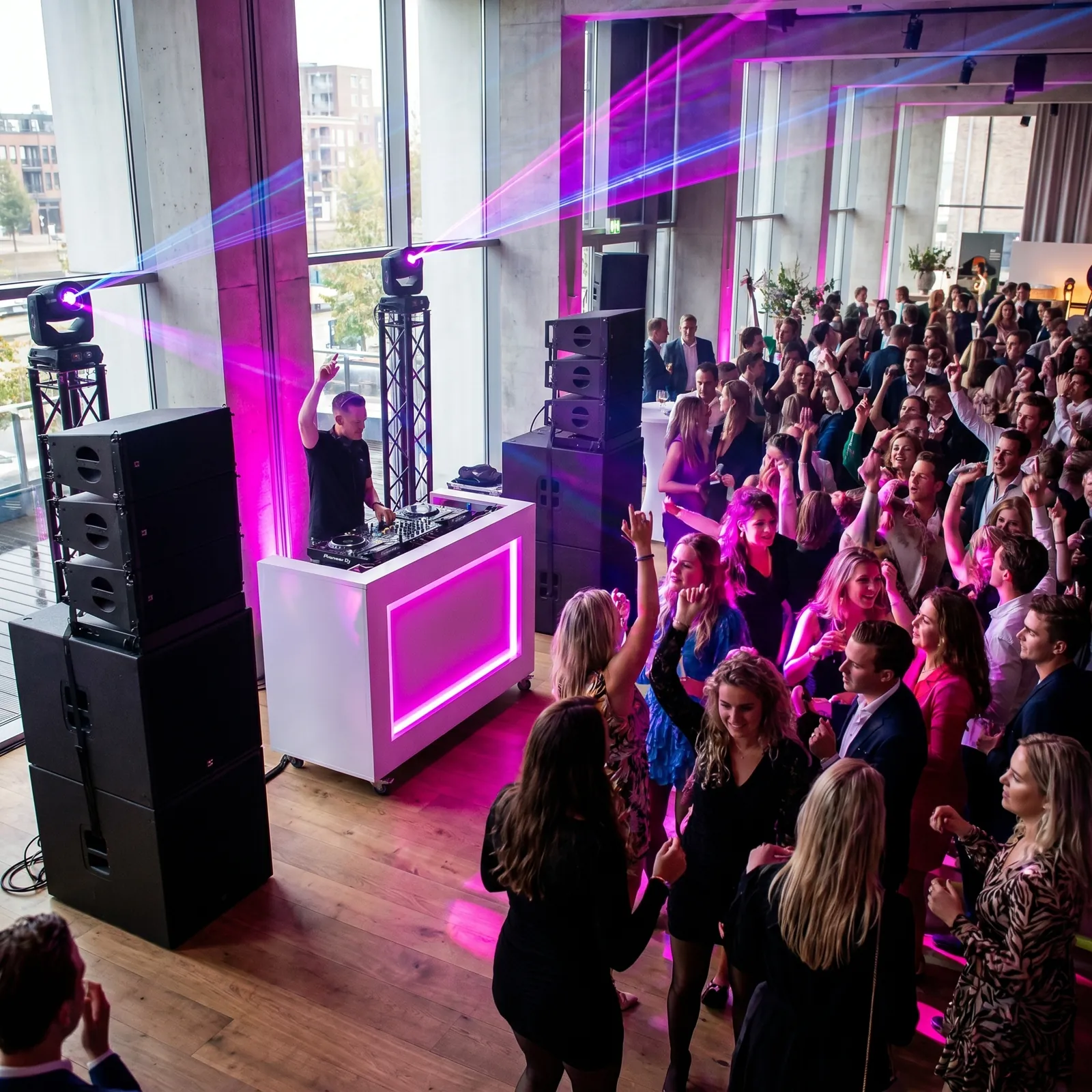 Grote feestlocatie met roze lasers, line-array en witte DJ-booth
